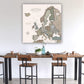 a large map of Europe hanging on a wall above a wooden dining table with chairs.