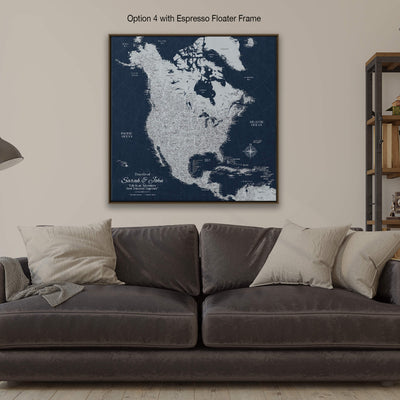 a large, detailed map of North America, with the countries and major cities clearly marked. The map is displayed on a wall above a gray couch, which is positioned in front of a bookshelf. The couch is adorned with two pillows, adding a touch of comfort to the scene. The overall setting appears to be a cozy living room or a similar space where people can relax and enjoy the view of the map.