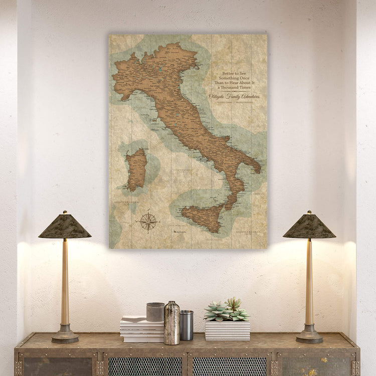 a large map of Italy hanging on a wall, with two lamps on a wooden table below it.