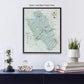a framed map of the Jackson Hole area, with a black floater frame, displayed on a wall above a blue dresser. The dresser has a glass dome containing a plant, a white clock, and a stack of books.