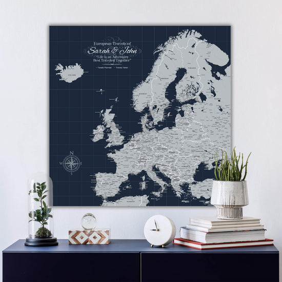 a large map of Europe on a wall, with a glass dome containing a plant and a stack of books on a blue shelf below it.