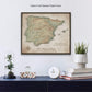 a framed map of Spain hanging on a wall, with a glass dome containing a plant and a stack of books below it.