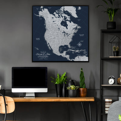 a large, detailed map of North America hanging on a wall above a wooden desk with a computer monitor, keyboard, and potted plants.