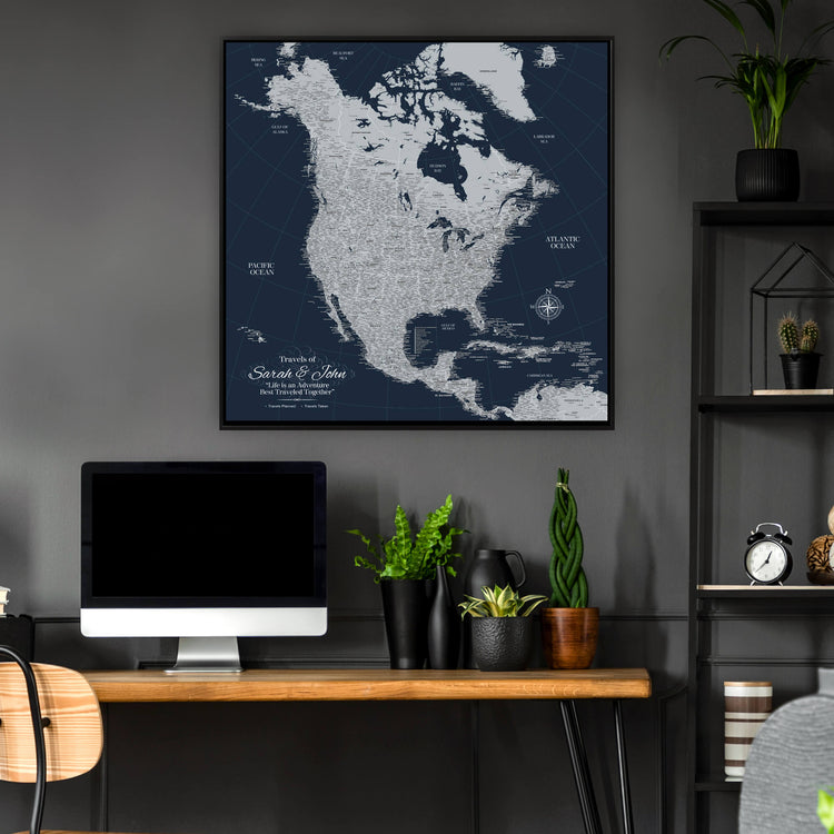 a large, detailed map of North America hanging on a wall above a wooden desk with a computer monitor, keyboard, and potted plants.