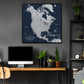 a large, detailed map of North America hanging on a wall above a wooden desk with a computer monitor, keyboard, and potted plants.