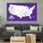 a large purple map of the United States with various locations marked, displayed on a wall above a gray couch and a wooden coffee table.
