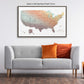a large framed map of the United States hanging on a wall above a gray sofa with orange and red throw pillows.