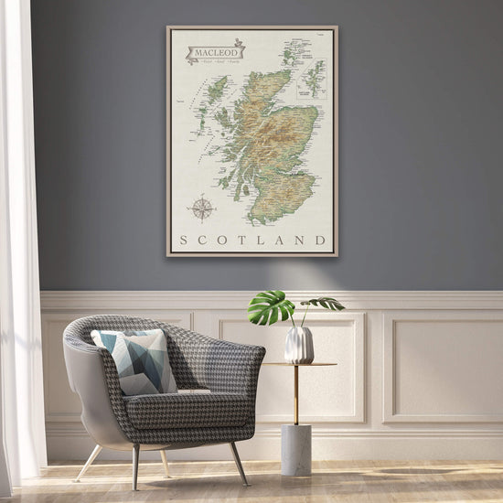 a framed map of Scotland hanging on a wall, with a gray armchair and a small side table with a plant in front of it.