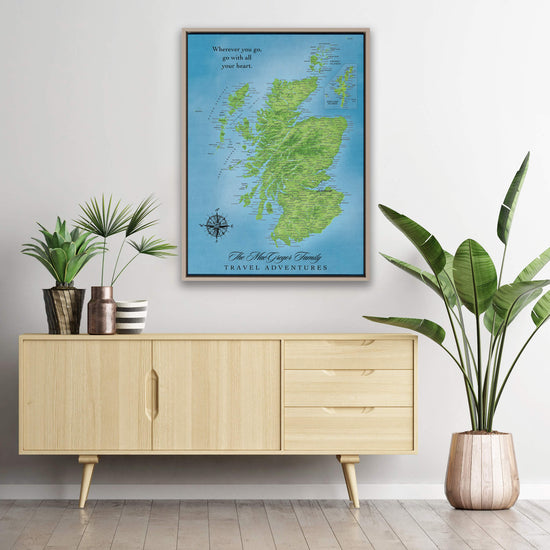 a large framed map of Scotland hanging on a wall, with a wooden cabinet below it and potted plants on either side.