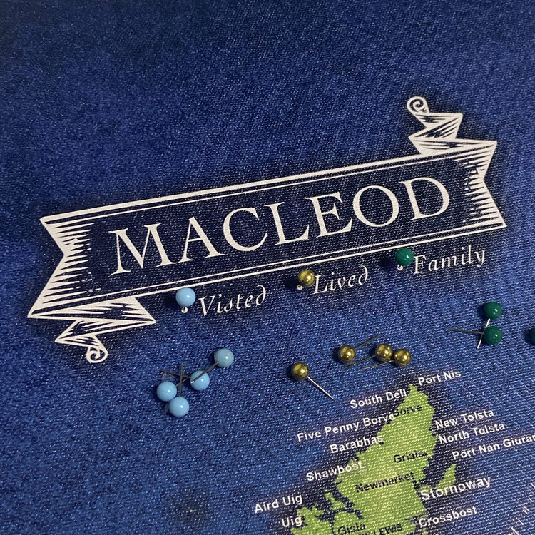 a blue fabric with a white banner that reads "Macleod" and a list of places, along with a few blue and green pins on the fabric.