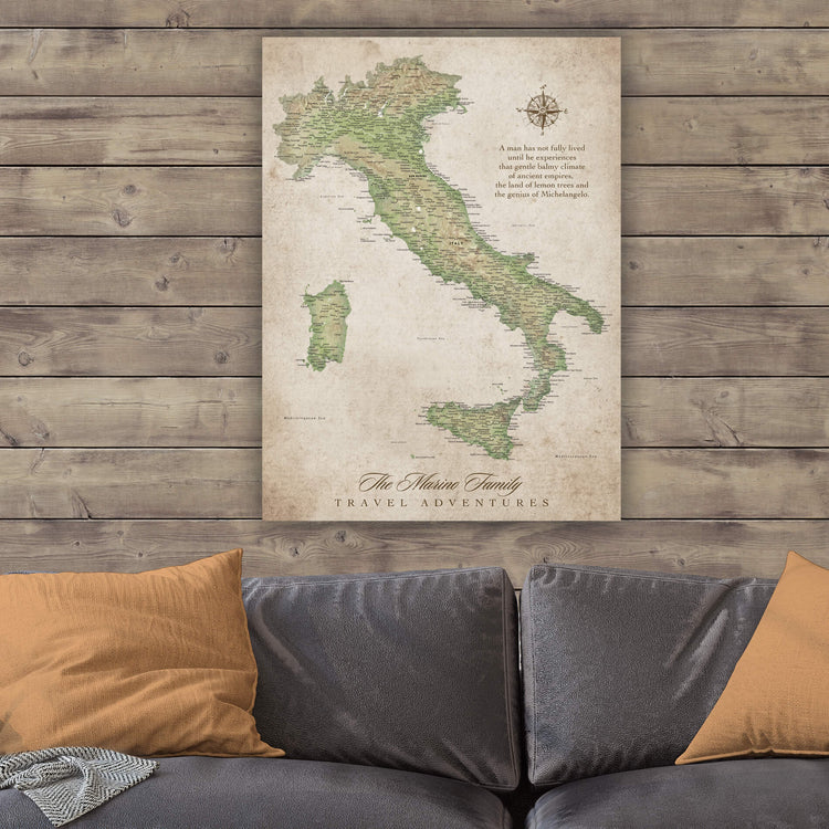 a large map of Italy hanging on a wooden wall above a gray couch with orange pillows.