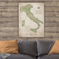 a large map of Italy hanging on a wooden wall above a gray couch with orange pillows.