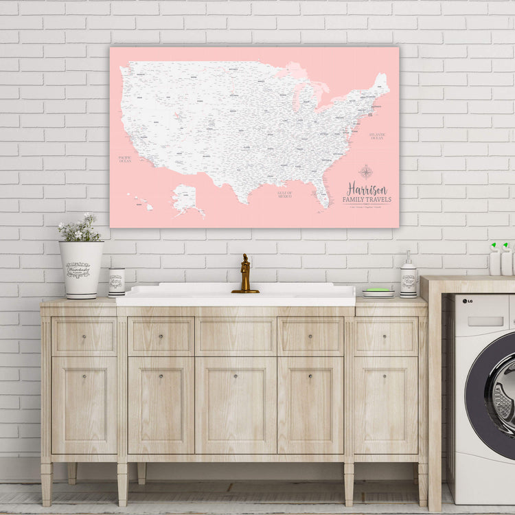 a bathroom vanity with a sink and a large map of the United States hanging above it. The map is pink and white, and it appears to be a scratch-off map of the U.S. The bathroom has a white sink and a washer, and there are some decorative items on the vanity.
