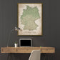 a large framed map of Germany hanging on a wall above a wooden desk with a laptop, a potted plant, and a lamp.