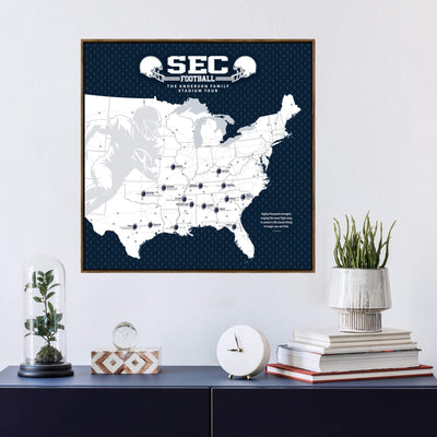 a framed map of the United States with various locations marked, along with a football helmet and a football. The map is set against a navy blue background, and there is a clock and a glass dome on a shelf below the frame.