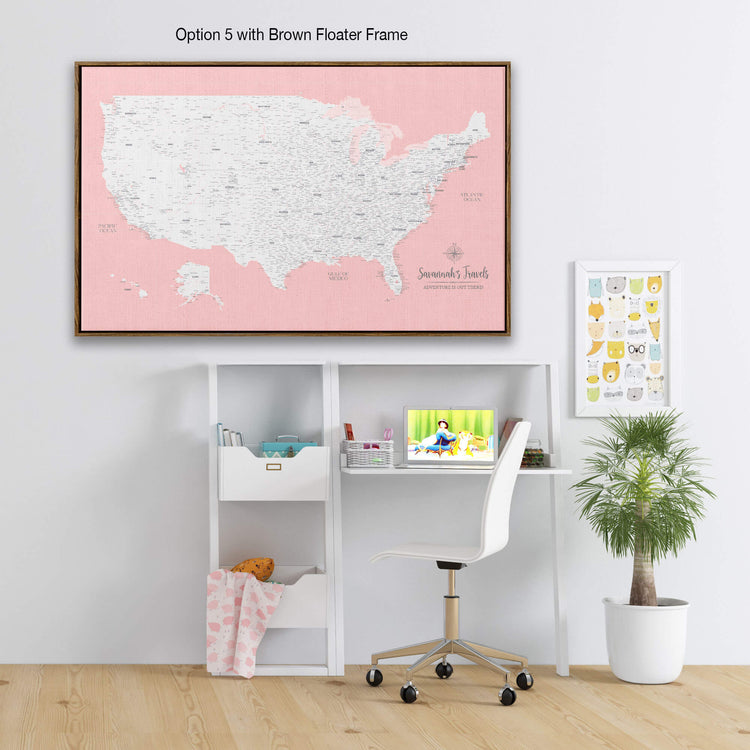 a workspace with a desk, chair, and various items such as a laptop, books, and a plant. Above the desk, there is a large map of the United States in a pink frame, and a smaller map of the world in a frame with a cartoon character on it.