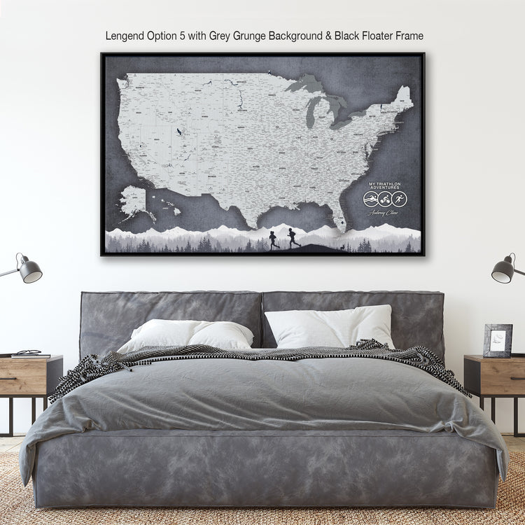 a large, black and white map of the United States with a grey grune background and a black floating frame. The map is mounted on a wall above a bed with a gray comforter and pillows.
