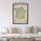 a framed vintage map of France hanging on a wall above a white couch with beige pillows.