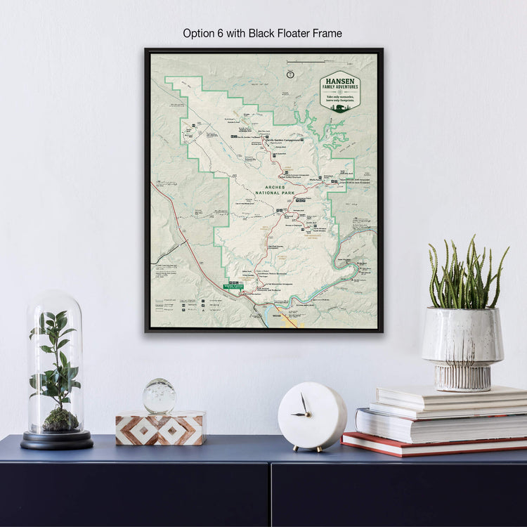a framed map of the Hanging Fork in the San Rafael Mountains, with a black floater frame. Below the map, there is a glass dome containing a plant, a white clock, and a stack of books.