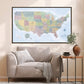 a large, colorful map of the United States hanging on a wall above a beige sofa in a living room.