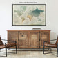 a large world map displayed on a wall above a wooden cabinet with four doors. The cabinet has a black frame and is positioned in front of two leather chairs.