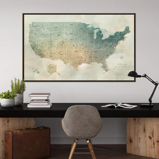 a large framed map of the United States hanging on a wall above a wooden desk with a chair, a lamp, and some books.