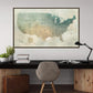 a large framed map of the United States hanging on a wall above a wooden desk with a chair, a lamp, and some books.