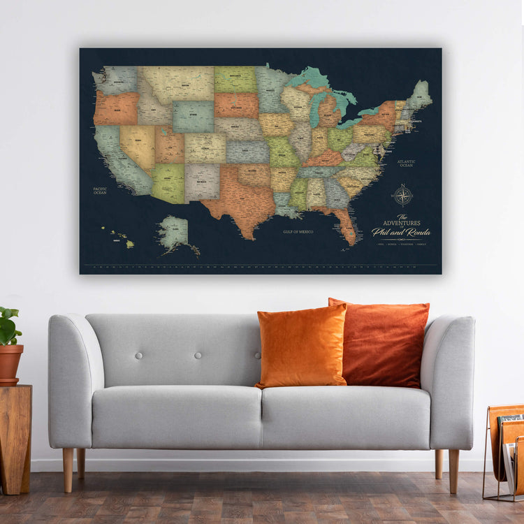 a large, detailed map of the United States hanging on a wall above a gray sofa with orange pillows.