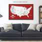 A large, custom map of the United States with various locations marked, displayed on a wall above a black couch with pillows.