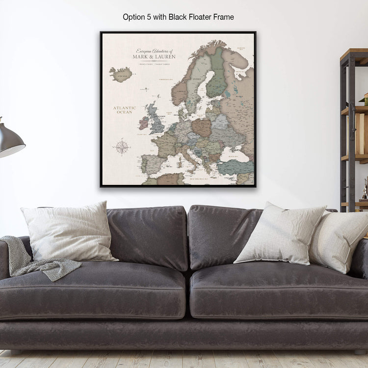 a large framed map of Europe hanging on a wall above a gray couch with white pillows.