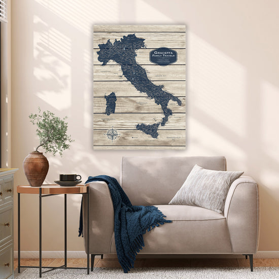 a cozy living room with a comfortable couch, a wooden side table, and a potted plant. Above the couch, there is a large map of Italy hanging on the wall, depicting the country in a unique wooden and blue design.