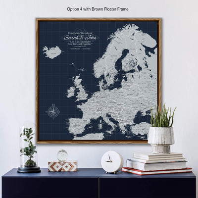 a large map of Europe with a brown frame, displayed on a wall above a wooden shelf. The map is surrounded by various decorative items, including a glass dome with a plant, a stack of books, and a white clock.