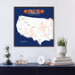 a framed map of the United States with various locations marked, including a football stadium, and the text "PAC 12 Football Stadium Tour" printed on it. Below the map, there is a small glass dome containing a plant, a white clock, and a stack of books.