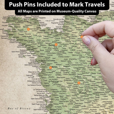 The image is a detailed map of France, with various locations marked and labeled. A hand is holding a pin, suggesting that the map is interactive and allows users to pin specific locations. The map is printed on a canvas, indicating that it is a printed representation rather than a digital image. The image is a collage of multiple images, and the caption provided is a brief description of the image without any redundancy or vague wording.