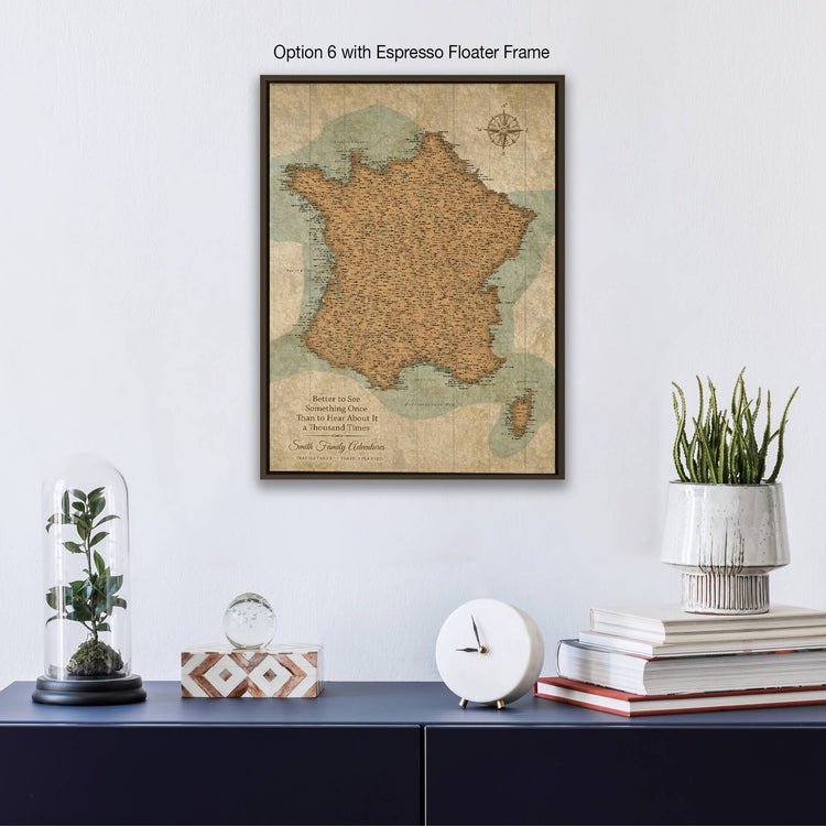 a framed map of France hanging on a wall, with a glass dome containing a plant and a stack of books below it.