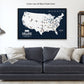 A large, custom map of the United States with various locations marked, displayed on a wall above a gray couch with white pillows.