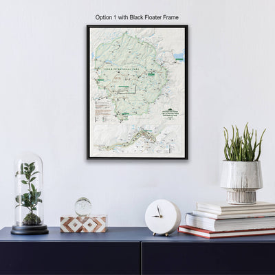 a framed map of Yosemite National Park hanging on a wall, with a glass dome containing a plant, a white clock, and a stack of books below it.